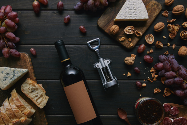 top view of wine bottle with blank label, corkscrew and various delicious snacks on wooden table  - Photo, Image