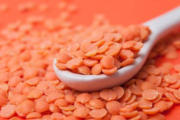 closeup of coral  lentils in a white porcelain spoon on orange background - Foto, Imagen