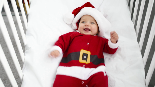 mother taking christmas ball from crib where lying adorable baby in santa costume - Πλάνα, βίντεο