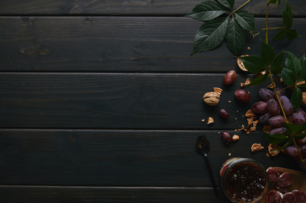 сверху вид на свежий спелый виноград, грецкие орехи, зеленые листья, варенье и нарезанную салями на деревянном столе
 - Фото, изображение