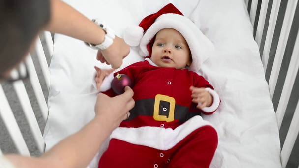 father giving christmas toy to adorable son in santa costume in crib at home, christmas concept - Footage, Video