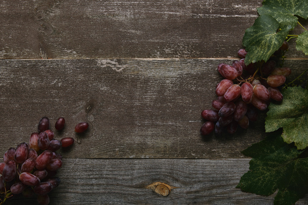 top view of fresh ripe grapes with green leaves on rustic wooden table - Photo, Image