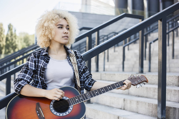 Pensive young afro american girl alone on city street playing guitar - Φωτογραφία, εικόνα