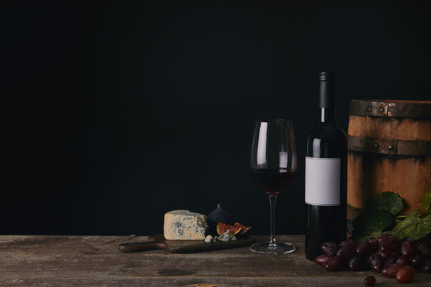 close-up view of glass, bottle and barrel of wine with cheese and grapes on black - Photo, Image