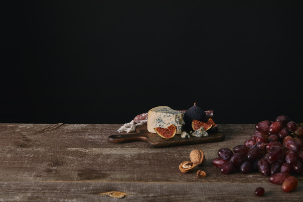 fresh ripe grapes, nuts and delicious cheese on wooden table on black - Photo, image
