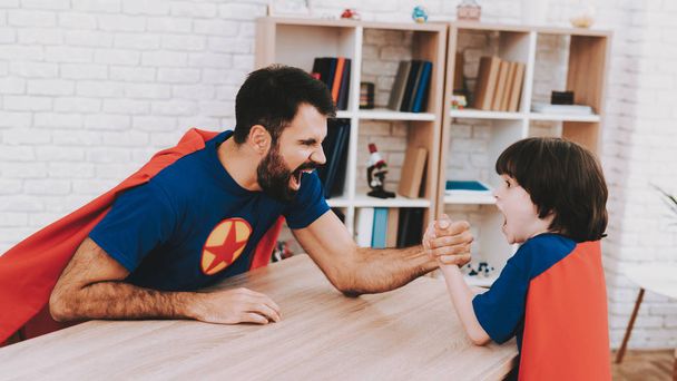 Father And Son. Red And Blue Superhero Suits. Arm Wresling Competition. Bright Room. Young Happy Family Holiday Concept. Resting Together. Healthy Lifestyle. Active Leisure. Holiday Joy. - Foto, Imagen