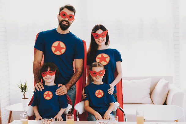 Young Happy Family In Superhero Suits. Dinner Concept. Masks And Raincoats. Bright Room. Resting Together. Juice And Cereals. Get Ready. Healthy Lifestyle. Parents Are Hanging Kids. - Photo, image