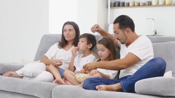 Happy family with two children relaxing at home, kids brother and sister watching a movie and having popcorn with parents - Materiał filmowy, wideo