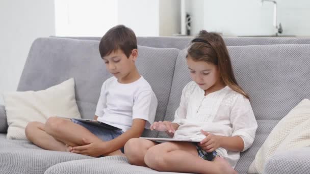 Two kids with gadgets. Sister and brother surfing the net or playing online games on digital tablets at home. Modern communication and gadget addiction concept. - Video