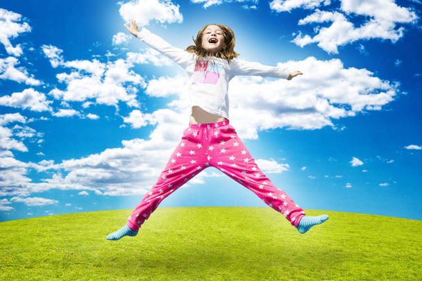 Щаслива дівчина стрибає високо на зеленій траві під час сонячного дня
. - Фото, зображення