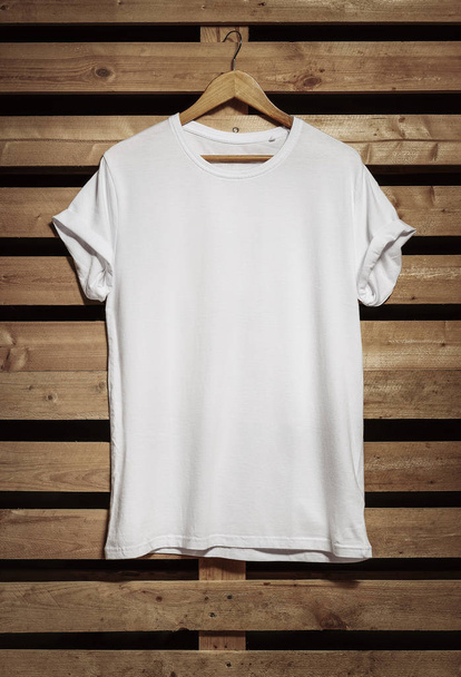 Blank white t-shirt hanging on the wooden background, with copy space  - Foto, Imagem