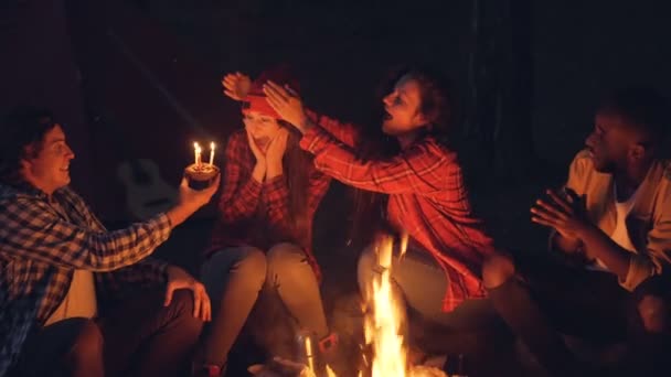 魅力的な若い女性のハイカーは、彼女の友人が手を拍手しながら蝋燭を吹くと叫びケーキを得て森林に誕生日を祝っています。お祝いと自然の概念. - 映像、動画