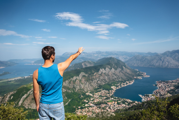 back view of man reaching out hand for Kotor bay and Kotor town in Montenegro - Photo, Image