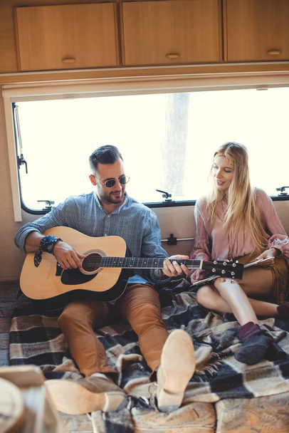 handsome man playing on guitar while girlfriend holding vinyl record inside trailer - Fotoğraf, Görsel