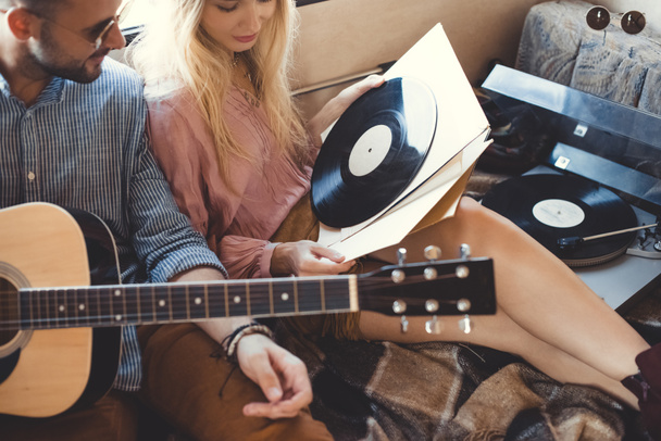 hippie couple with acoustic guitar and vinyl records sitting inside trailer - Photo, Image