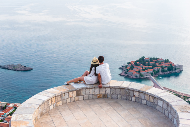 couple hugging on viewpoint and looking at island of Sveti Stefan in Budva, Montenegro  - Photo, Image