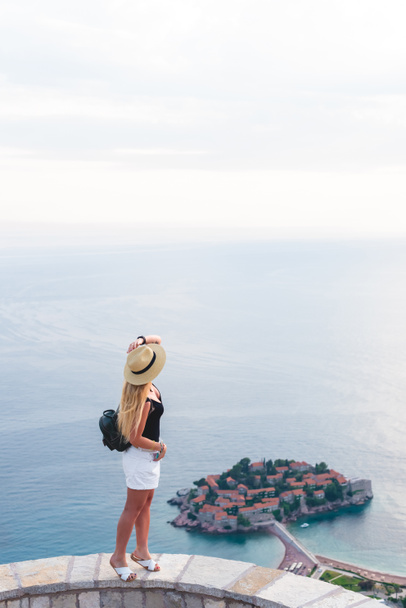 woman standing on viewpoint and looking at saint stephen island in Adriatic sea, Budva, Montenegro  - Photo, Image
