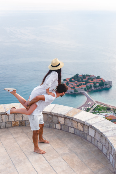 Chłopak, dając piggyback dziewczyna w viewpoint w pobliżu wyspy Sveti Stefan w Budva, Czarnogóra - Zdjęcie, obraz