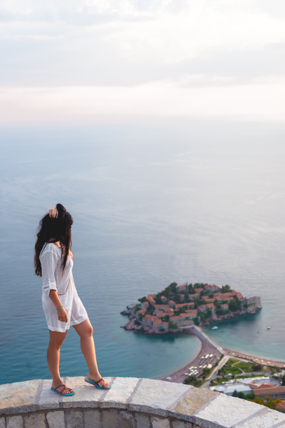 Widok z boku kobiety, patrząc na wyspie Sveti Stefan z resort hotel w Adriatyku, Budva, Czarnogóra - Zdjęcie, obraz