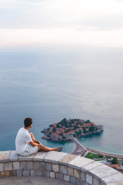 homme assis sur le point de vue et regardant l'île de Sveti Stefan avec hôtel station balnéaire en mer Adriatique, Budva, Monténégro
 - Photo, image