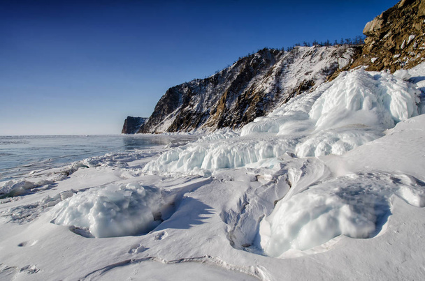 Lake Baikal is covered with ice and snow, strong cold, thick clear blue ice. Icicles hang from the rocks. Lake Baikal is a frosty winter day. Amazing place - Photo, Image