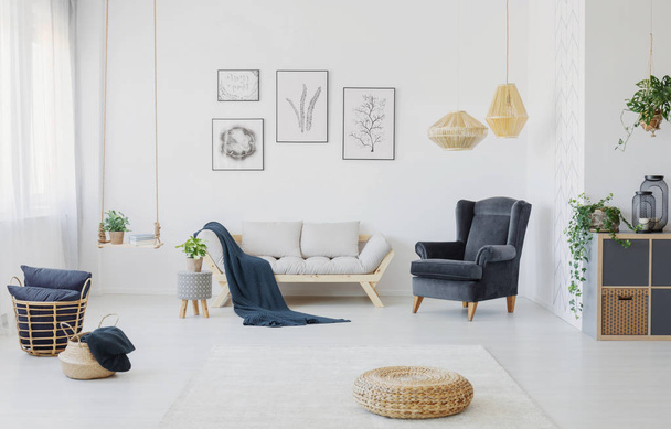 Real photo of a living room interior with a sofa, armchair, posters on a wall and wicker pouf - Фото, изображение