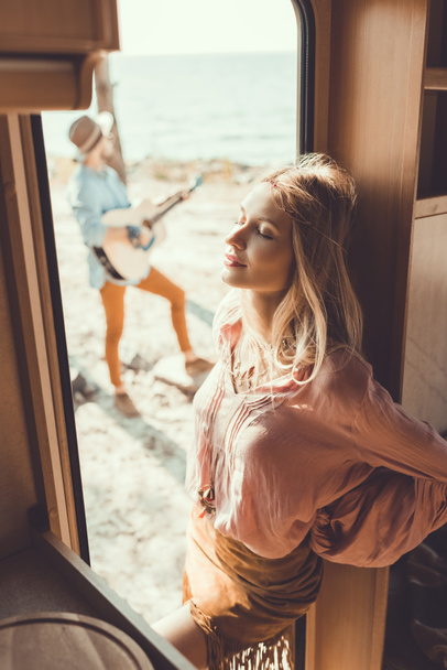 selective focus of girl standing in door of trailer and listening man playing guitar - Zdjęcie, obraz
