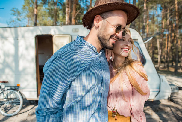 hippie couple embracing near trailer in forest - Foto, afbeelding