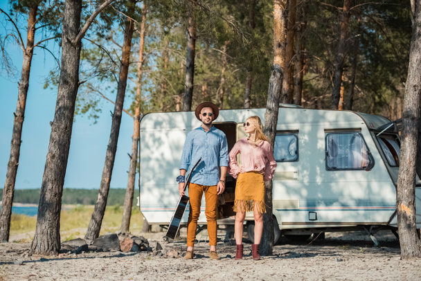 joven hippie pareja con acústica guitarra posando cerca campervan
 - Foto, Imagen