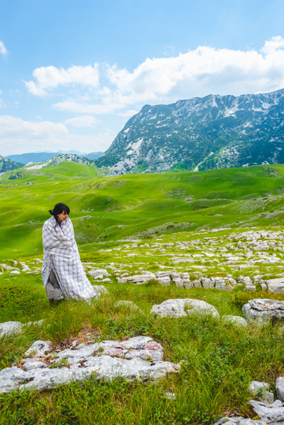 attractive woman in blanket standing on green valley in Durmitor massif, Montenegro - Photo, Image