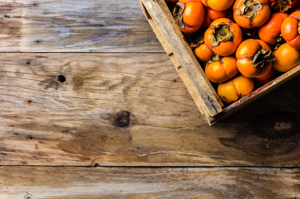 Box of fresh fruits persimmon kaki on old wooden background. Copy space - Foto, Imagem