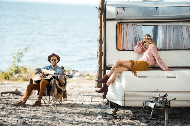 hippie fille assis sur camping-car tandis que l'homme jouer de la guitare acoustique près
 - Photo, image