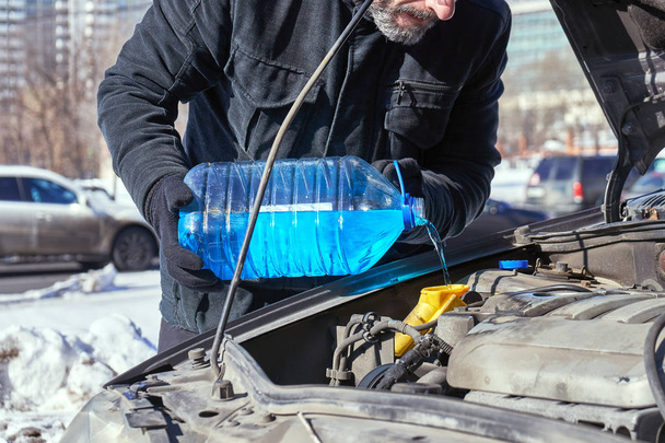 Homme remplissant un réservoir de lave-glace d'une voiture par antigel
 - Photo, image