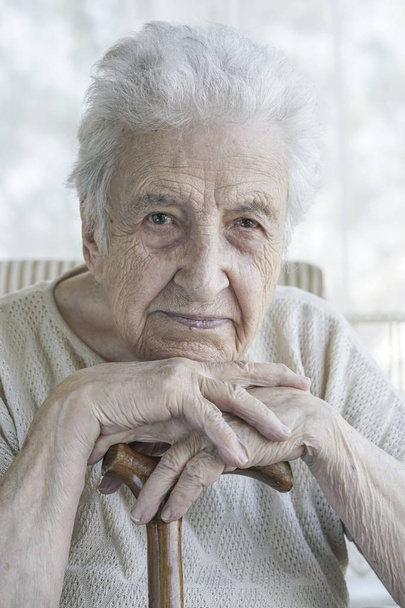 A lovely senior woman lean in on a wooden cane at home - Foto, imagen