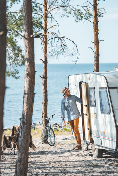 handsome man in hat in camp with trailer and bicycle - Valokuva, kuva