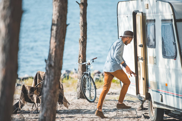 young man going into trailer in camp with bicycle near the sea - Valokuva, kuva