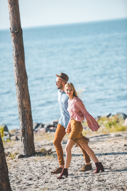 belo casal hippie de mãos dadas e andando na natureza perto do mar
 - Foto, Imagem