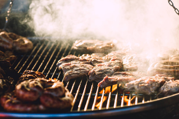 Κρέας και τα λουκάνικα είναι τηγανητά σε μεγάλη σχάρα στην καφετέρια του δρόμου. - Φωτογραφία, εικόνα