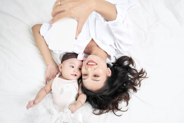 Kadın bir bebekle ahşap yerde yatarken bir selfie yapıyor - Fotoğraf, Görsel