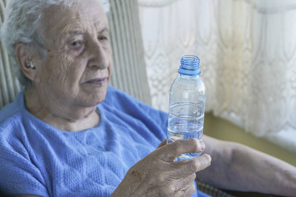 Старша жінка тримає пляшку питної води
 - Фото, зображення