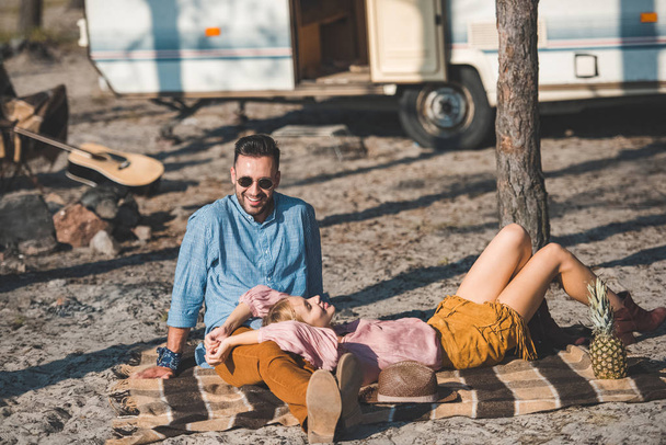 hippie couple relaxing on blanket near trailer in nature - Фото, изображение
