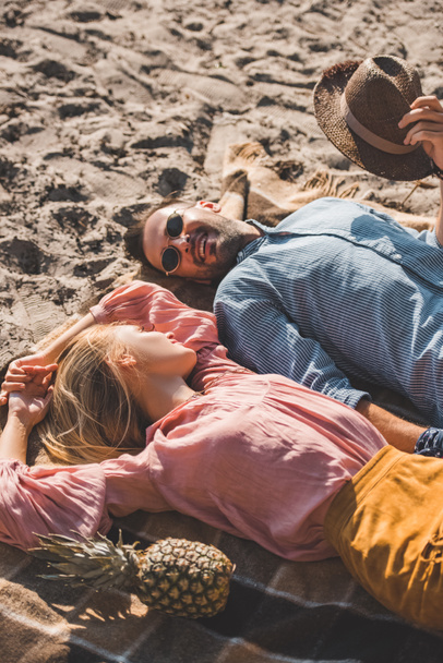 hippie couple looking at each other and relaxing on blanket on sand - Photo, Image