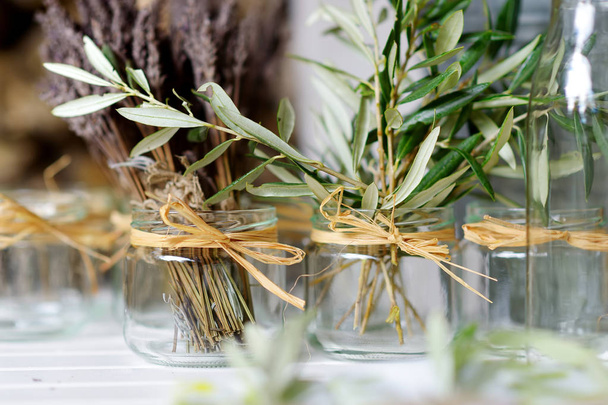 Fresh olive branches and dried lavender in square glass vases on a wooden table at home - Photo, Image