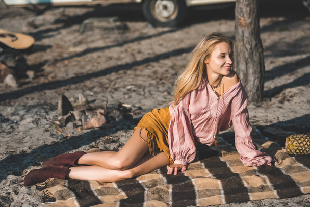 attractive happy girl sitting on blanket with pineapple near trailer in nature - Photo, Image
