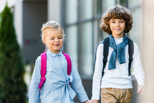 cute preteen schoolchildren with backpacks holding hands and walking together - Photo, Image