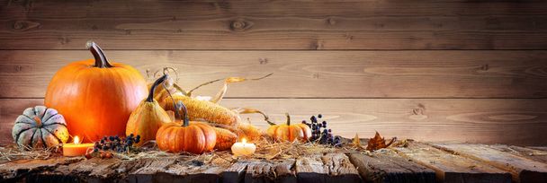 Kiitospäivän tausta - kurpitsat maissintähkällä ja kynttilöillä maalaismaisen puisen pöydän päällä
 - Valokuva, kuva
