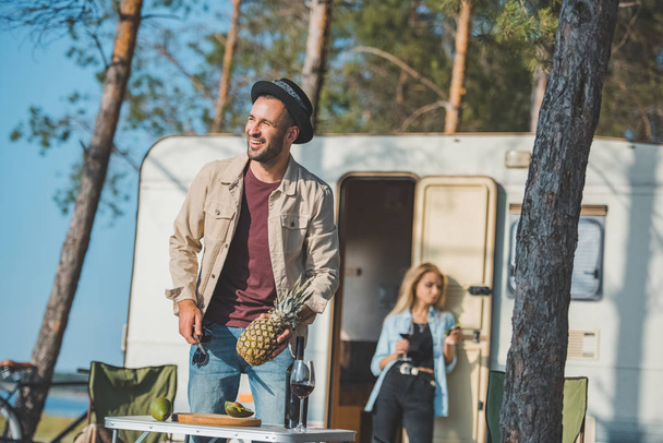 selective focus of man cutting pineapple while woman with wine standing at trailer behind - Фото, зображення