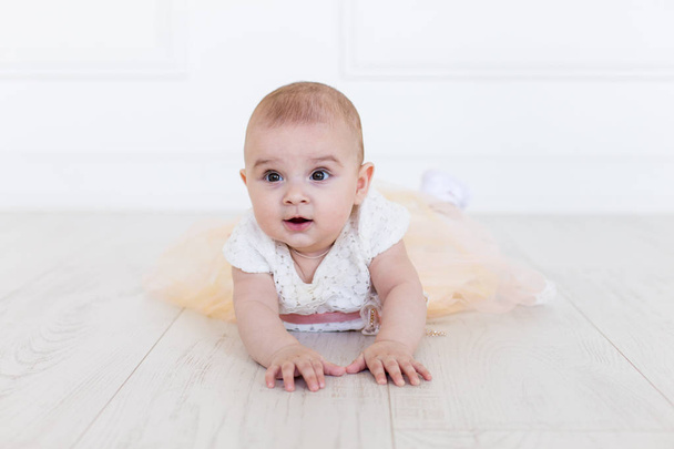 A baby girl is crawling along the floor with an inquisitive and wondering look on her face. Horizontal shot. - Fotografie, Obrázek
