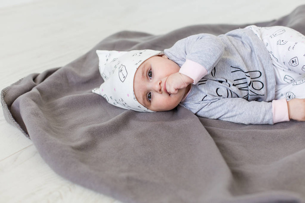 Cute baby lying on a grey blanket and keeps fingers in his mouth. Happy childhood concept. - Foto, immagini