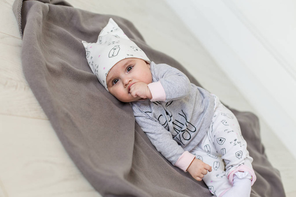 Cute baby lying on a grey blanket and keeps fingers in his mouth. Happy childhood concept. - Foto, afbeelding